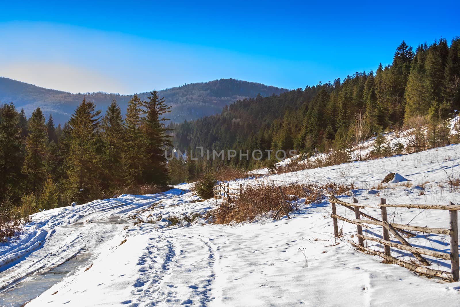 wooden fence near the road leading to the forest in the winter mountains in good weather