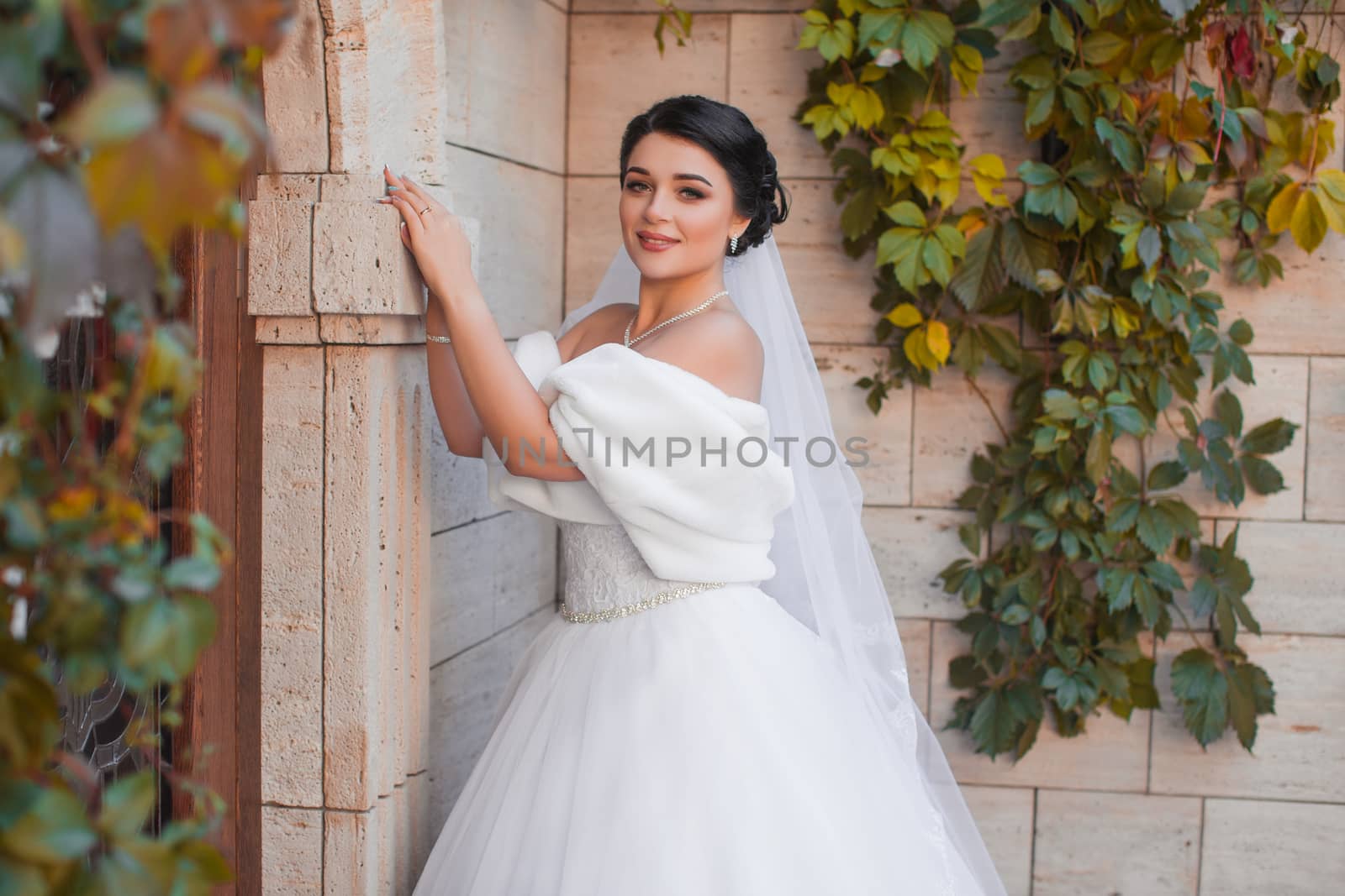 Stylish bride stands by the brick wall, posing on the photo