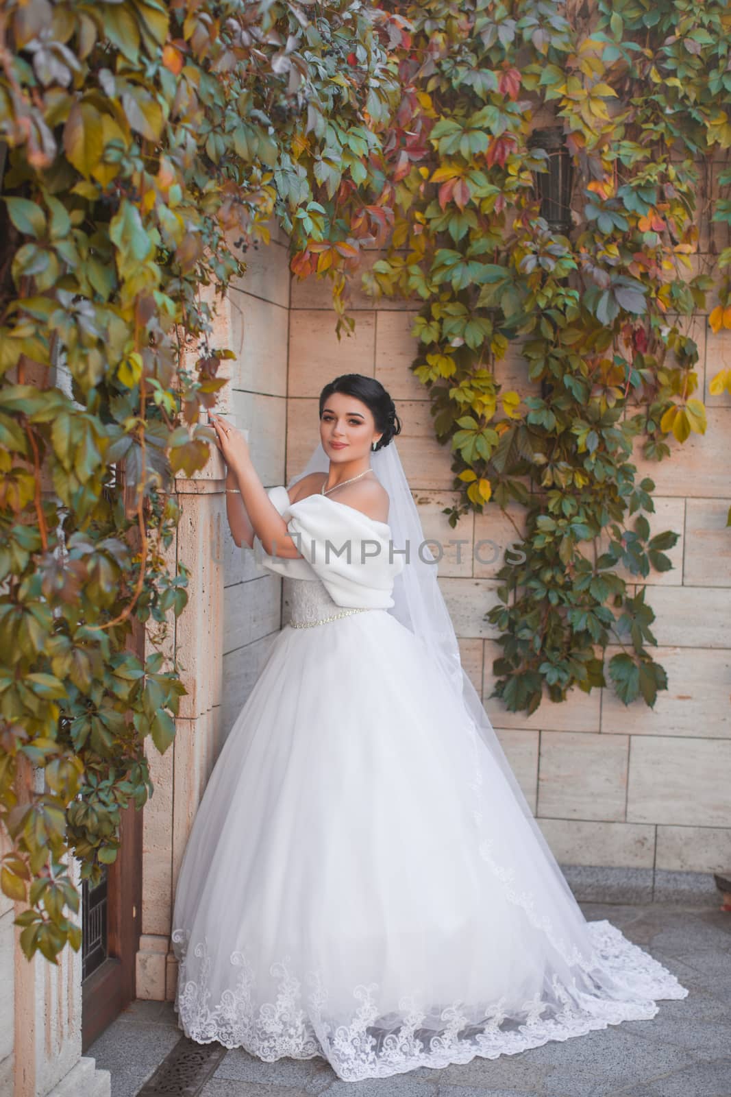 Stylish bride stands by the brick wall, posing on the photo