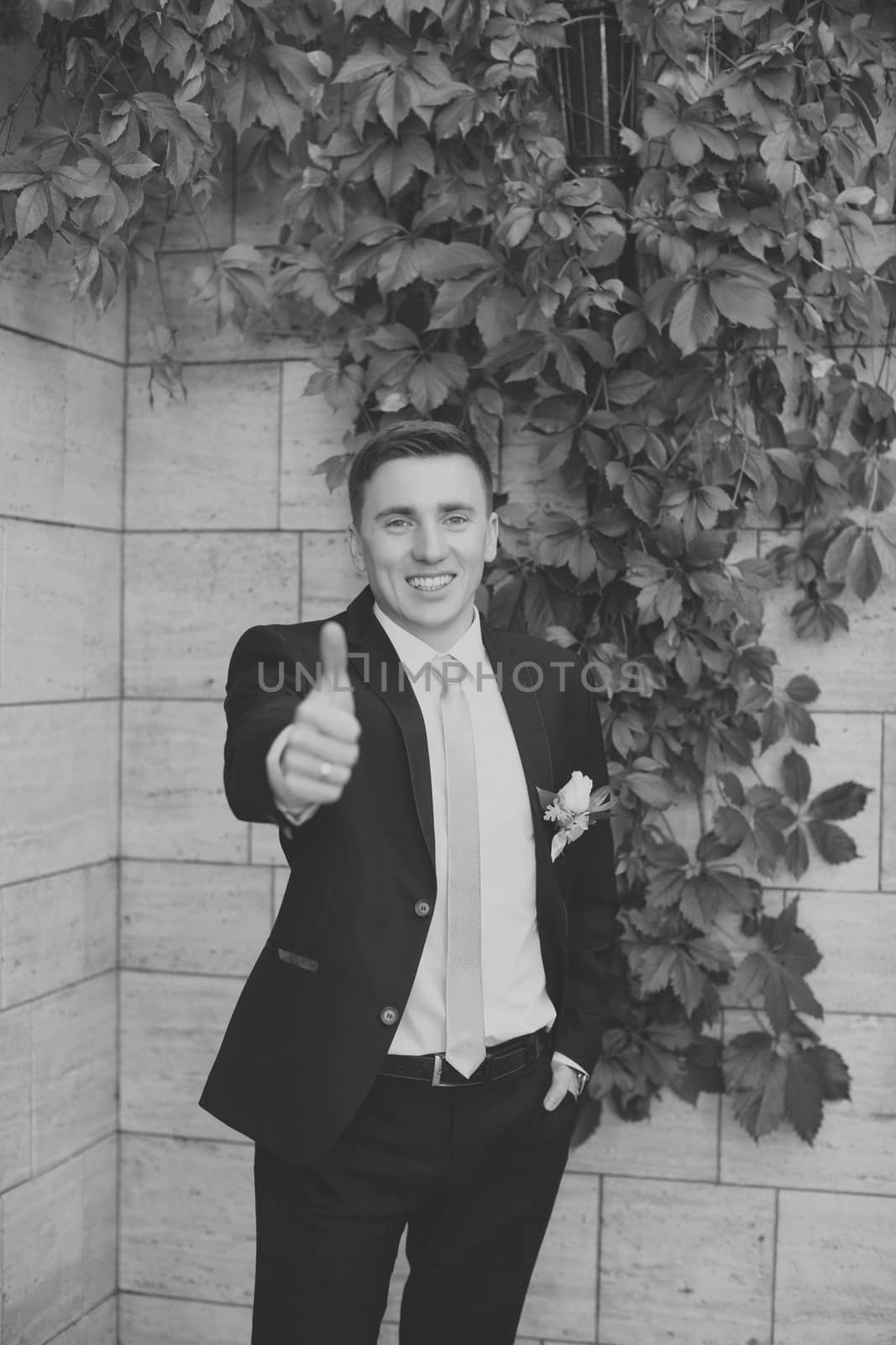 Happy bridegroom in a stylish suit against a brick wall background