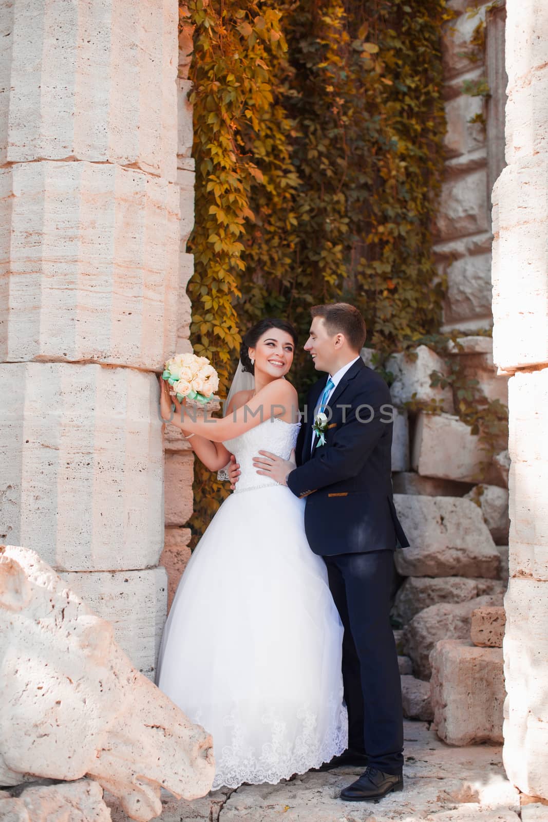 The groom tenderly embraced the happy bride standing at the column