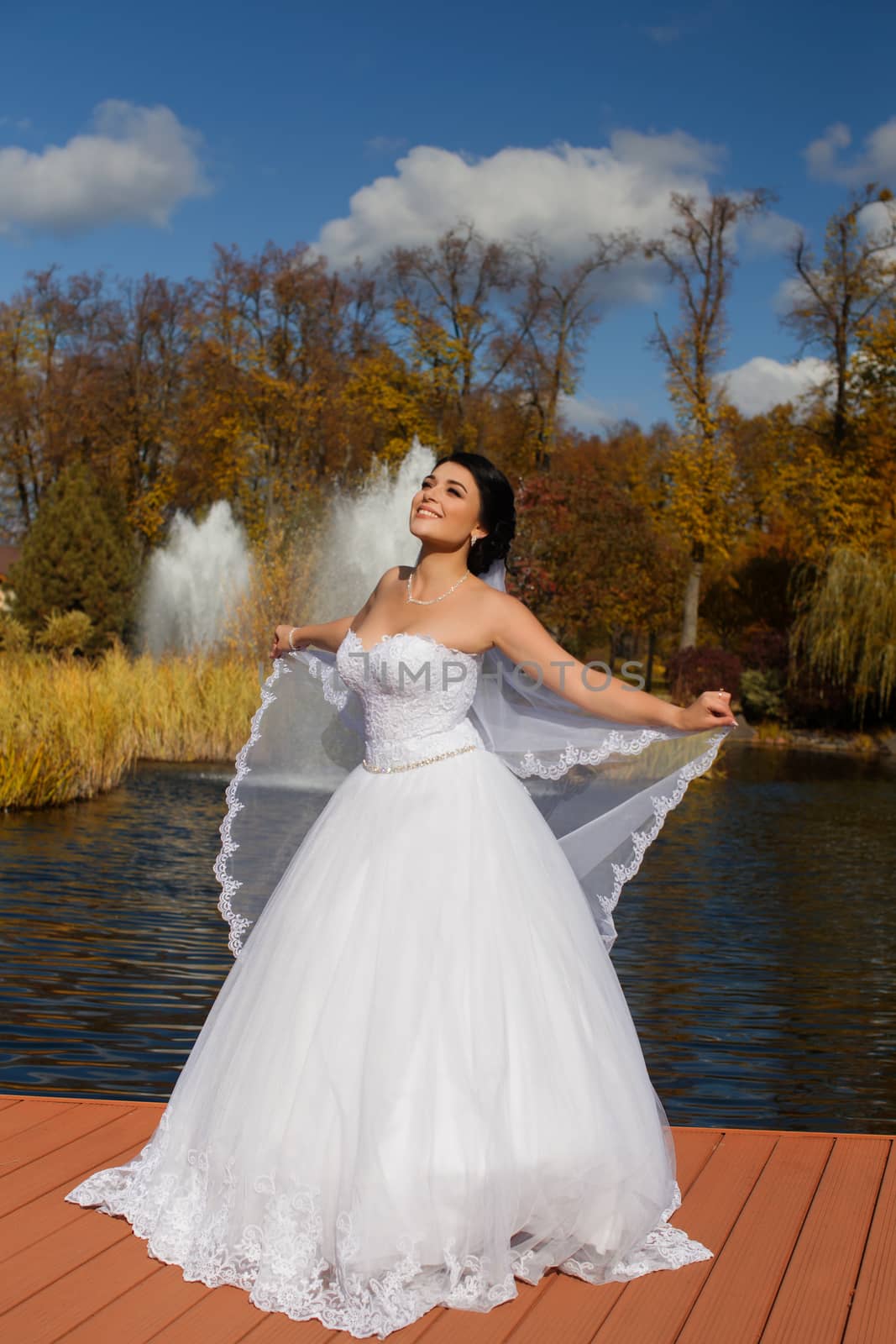 A happy bride in a rich wedding dress is standing on the pier