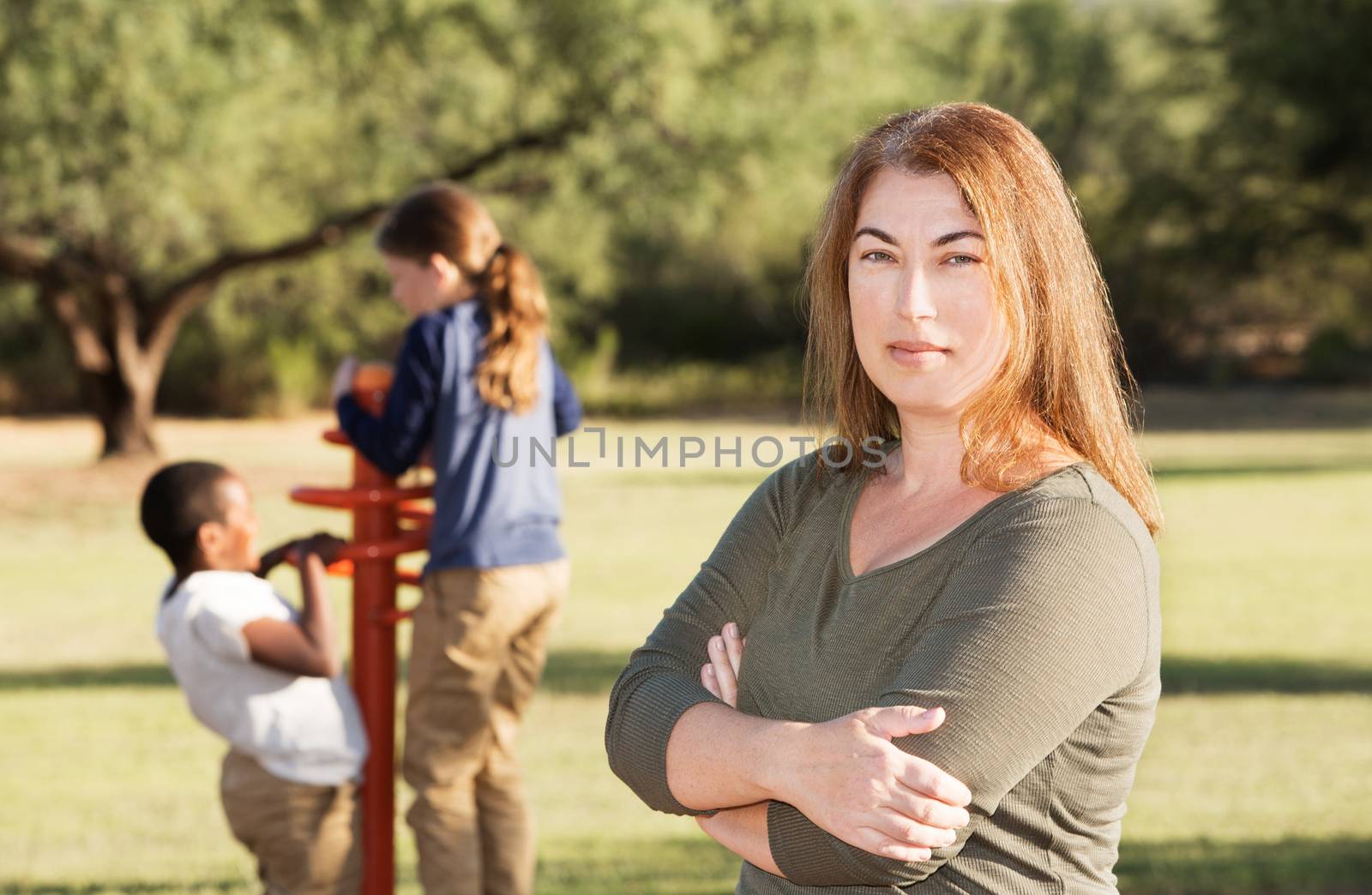 Single mother standing in front of two children playing behind her