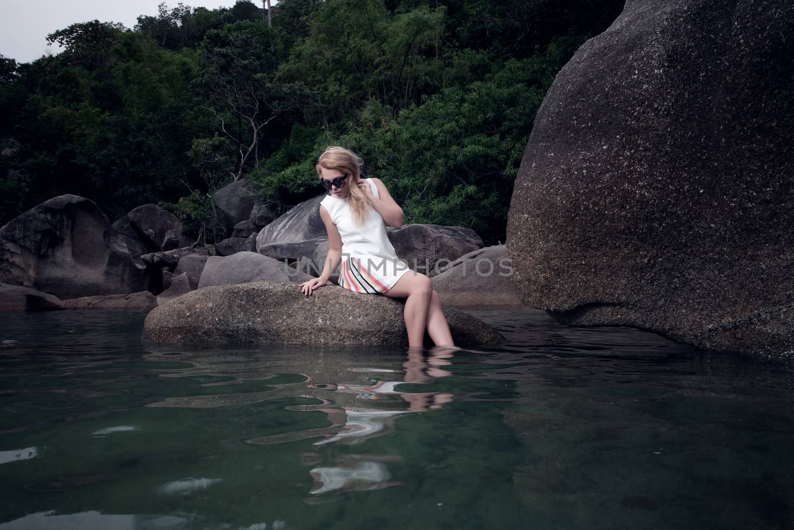 portrait of girl sitting on rock and looking on water