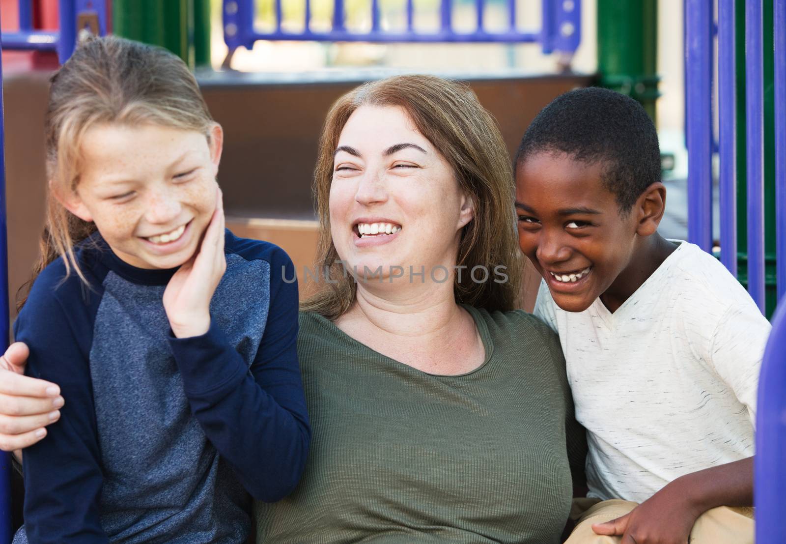 Laughing mother embracing two giggling young sons at park outside