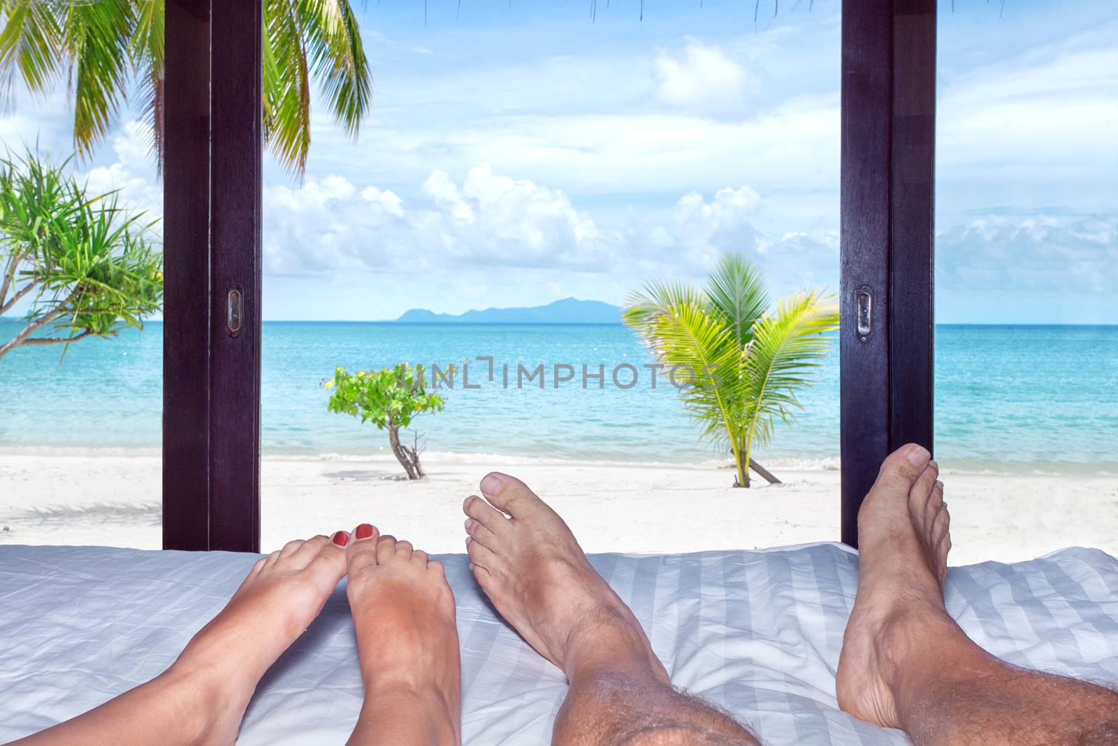 Close up view of man's and woman's legs on the bed in tropical resort