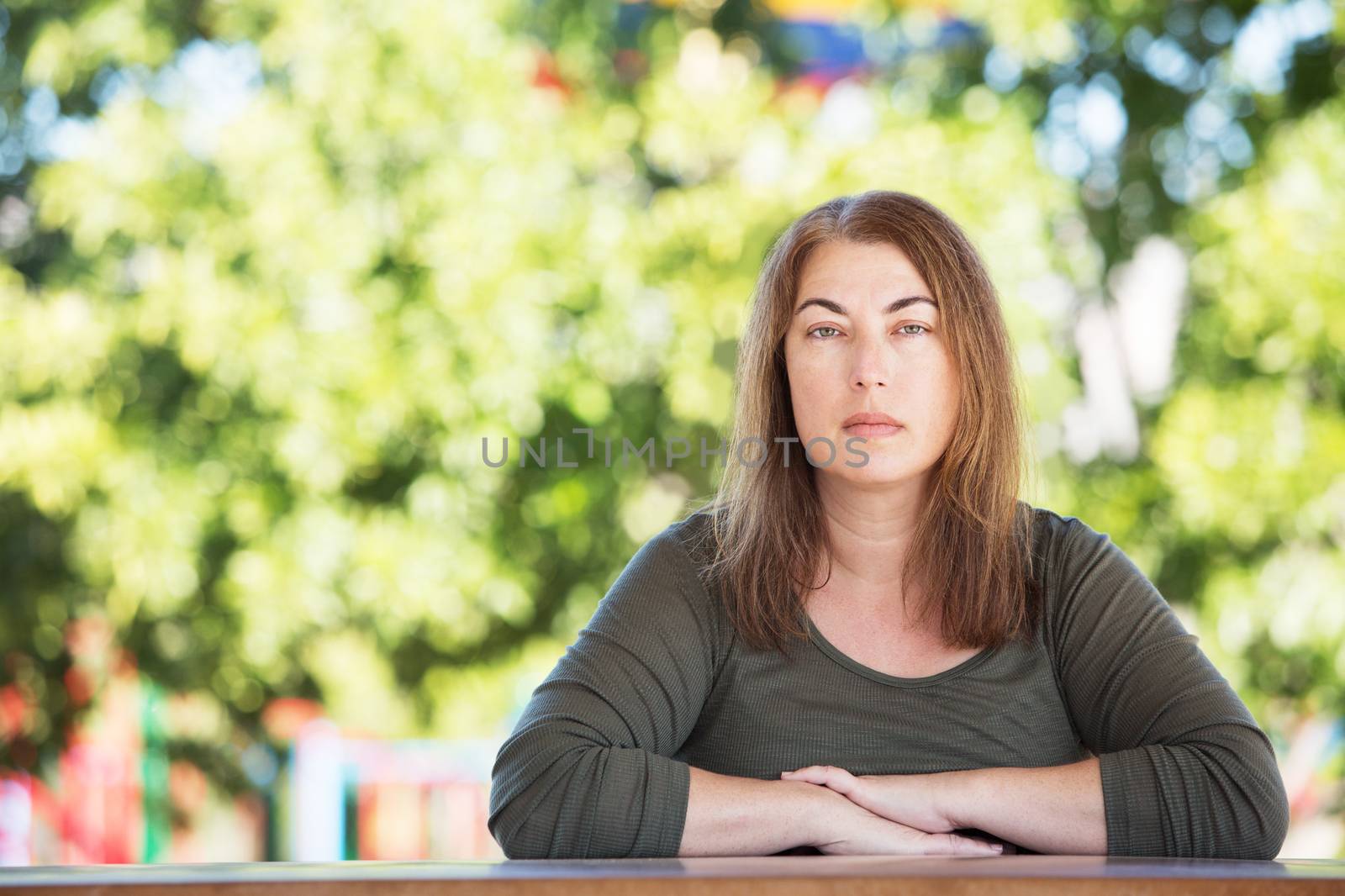 Serious adult female with folded arms seated at table outside