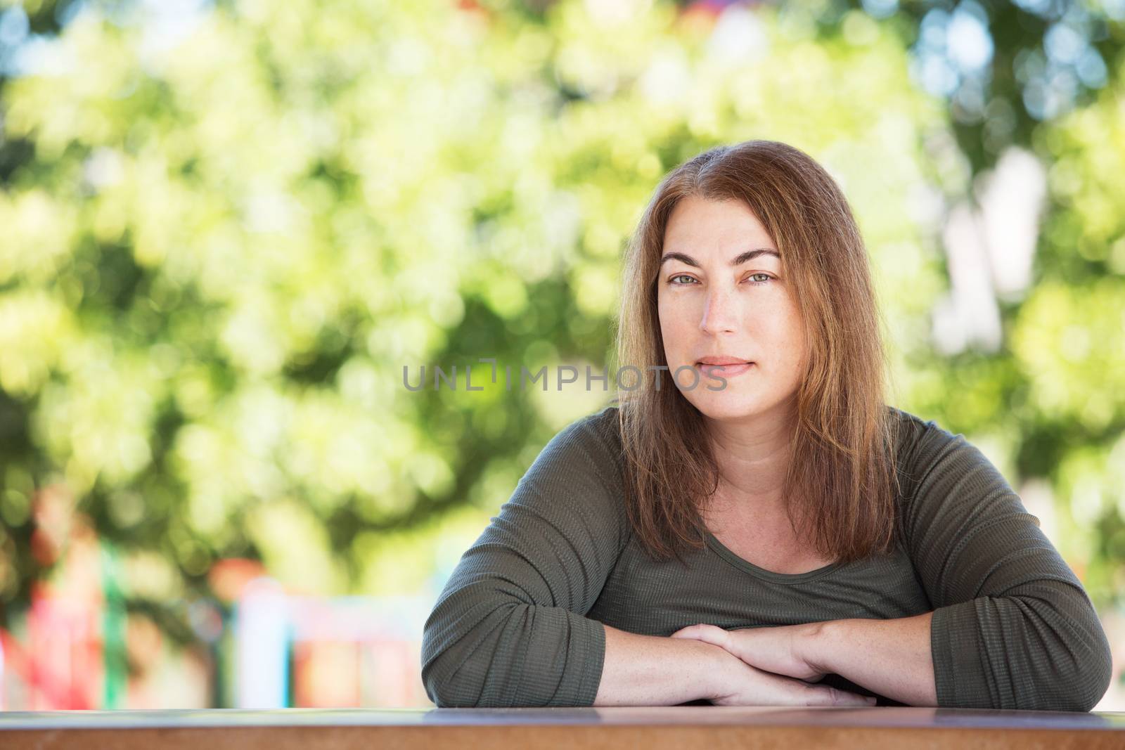 Pretty single adult female with folded arms seated at table with tree in background