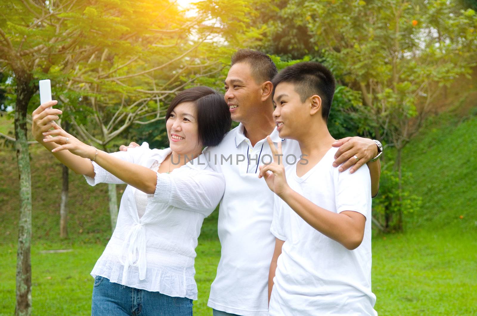 happy asian family taking a outdoor selfie in a city park.