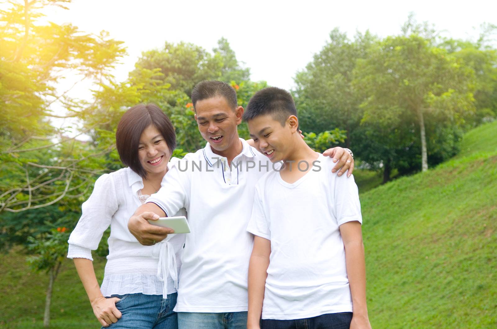 happy asian family taking a outdoor selfie in a city park.