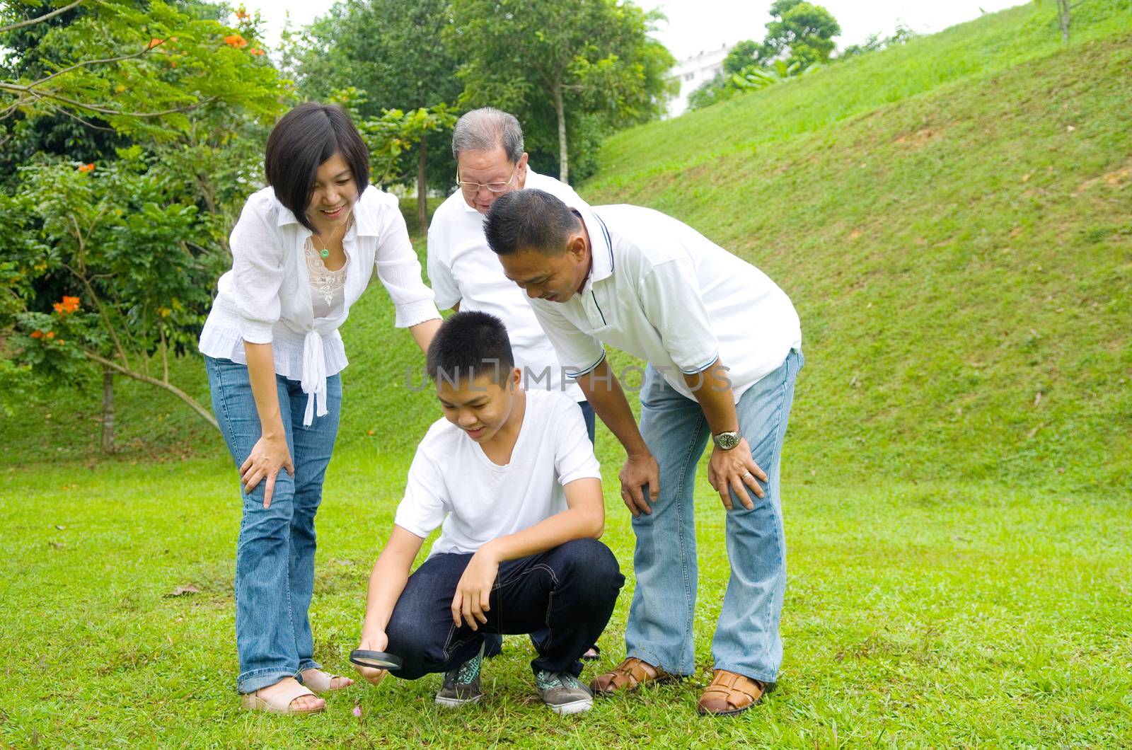 Asian three generation family inspecting leaf with magnifying glass in the park. Healthy lifestyle concept.