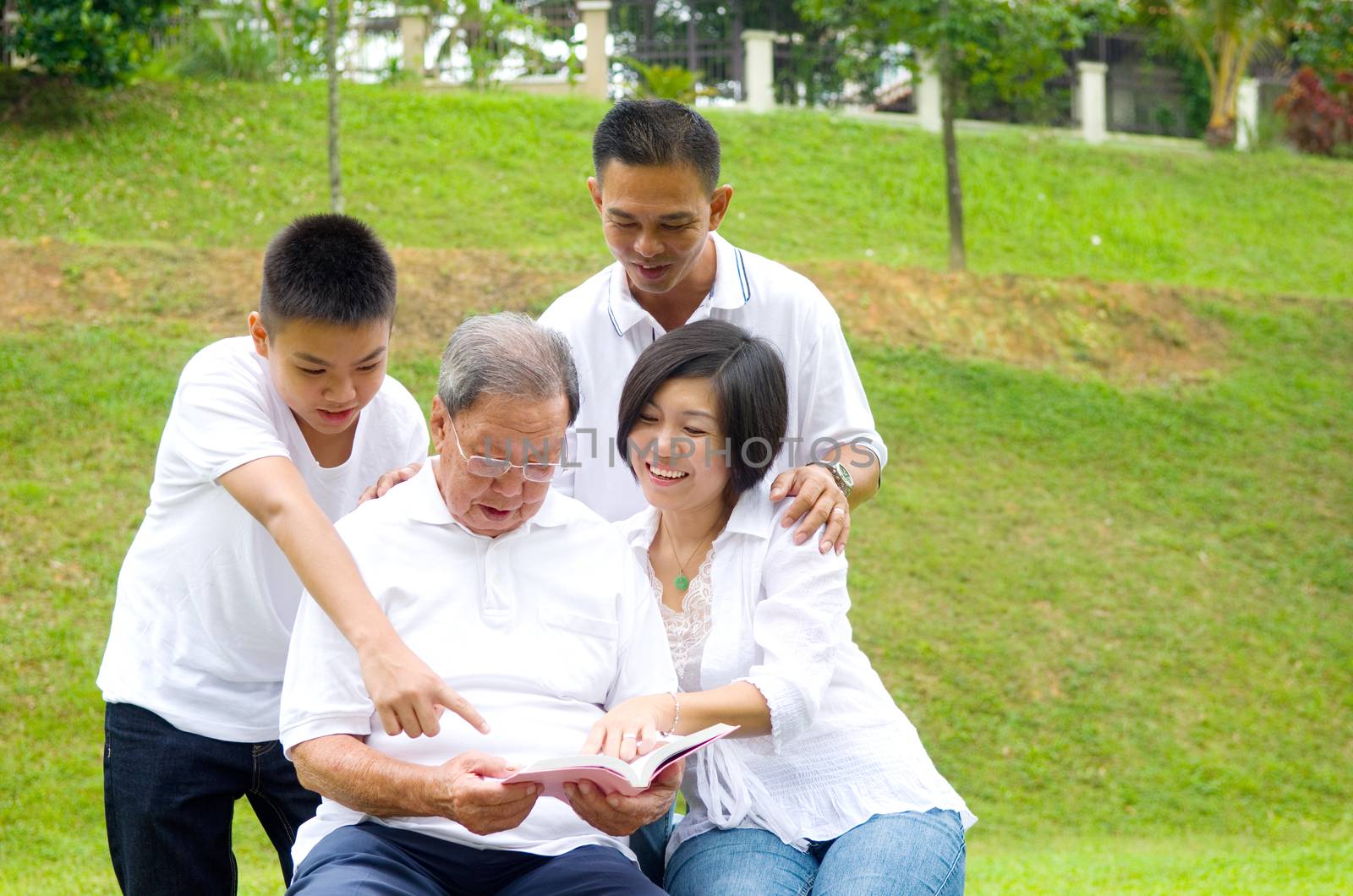 Asian three generation family reading book at outdoor park