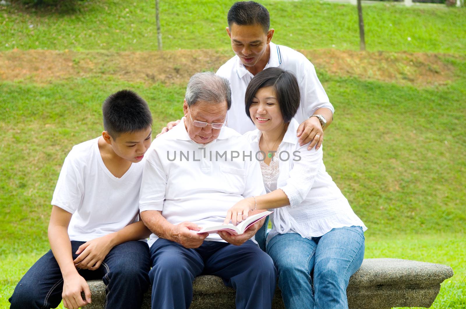 Asian three generation family reading book at outdoor park