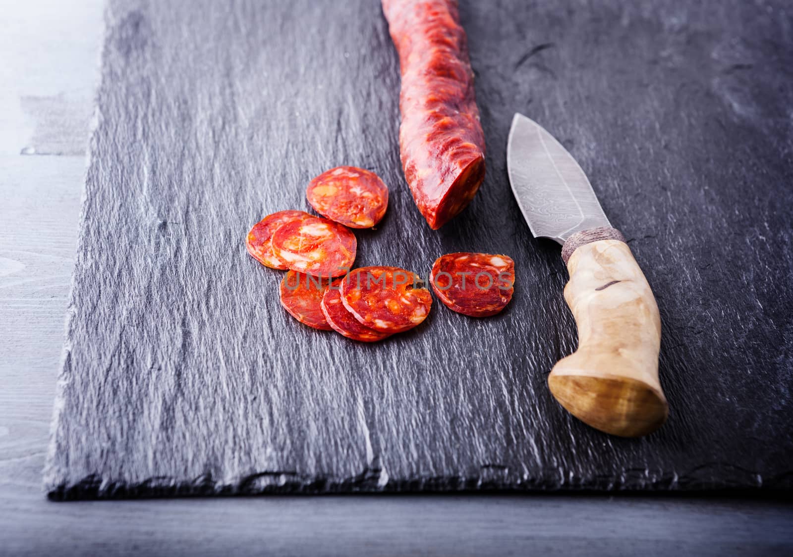 Spanish chorizo with a knife on a stone plate. by supercat67