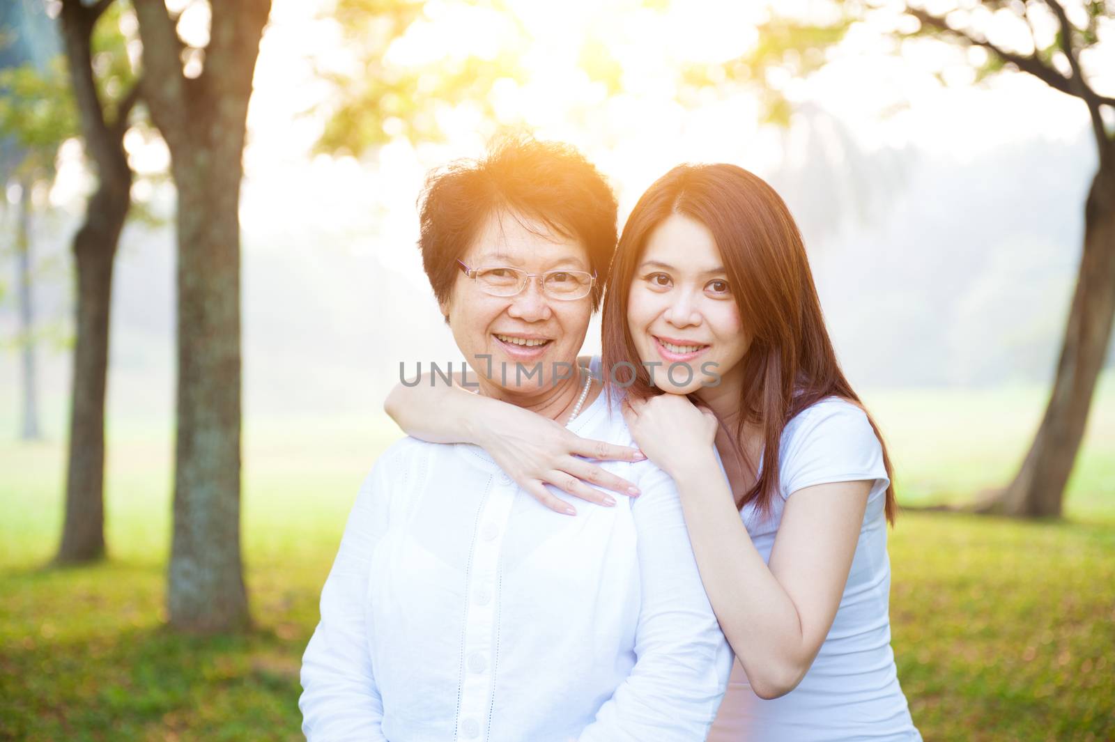 Portrait of Asian elderly mother and daughter, senior adult woman and grown child. Outdoors family at nature park with beautiful sun flare.