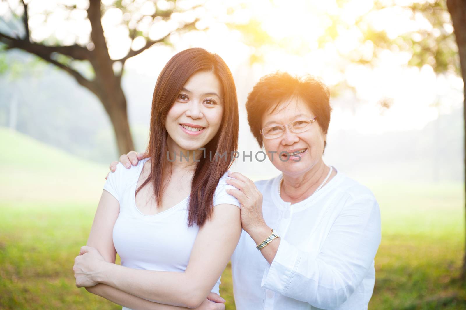 Portrait of beautiful Asian elderly mother and daughter, senior adult woman and grown child. Outdoors family at nature park with beautiful sun flare.
