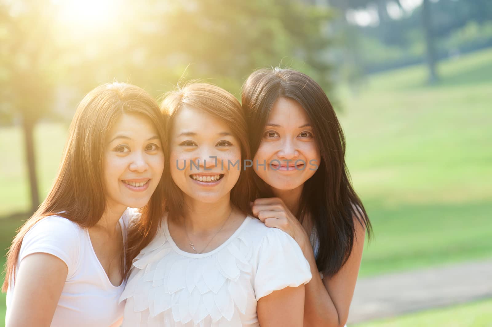 Group of young Asian females having fun at outdoor park, looking at camera smiling happily, sisters or girlfriends, friendship concept, sun flare background.