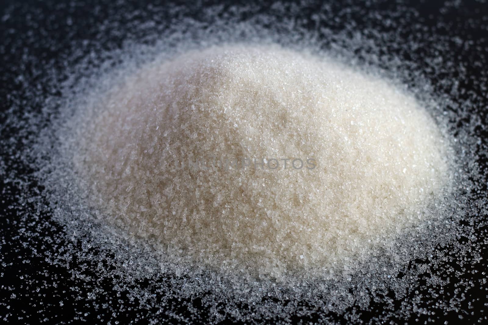 Sweet sugar or salt heap on black background. Bunch of spilled white sand sugar