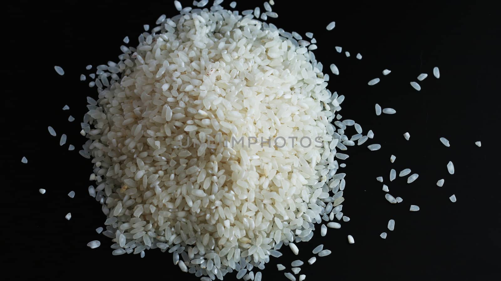 Round pile heap of rice or wholegrain spill on black background. Agriculture food raw seed. Closeup macro photo
