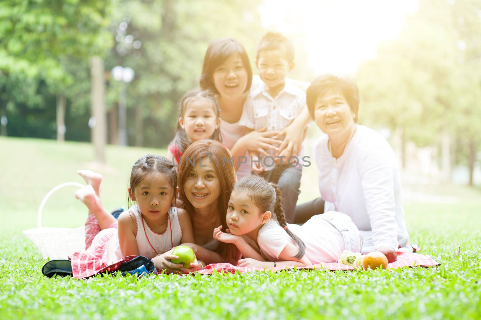 Asian multi generations family portrait, grandparent, parents and children, outdoor nature park in morning with sun flare.