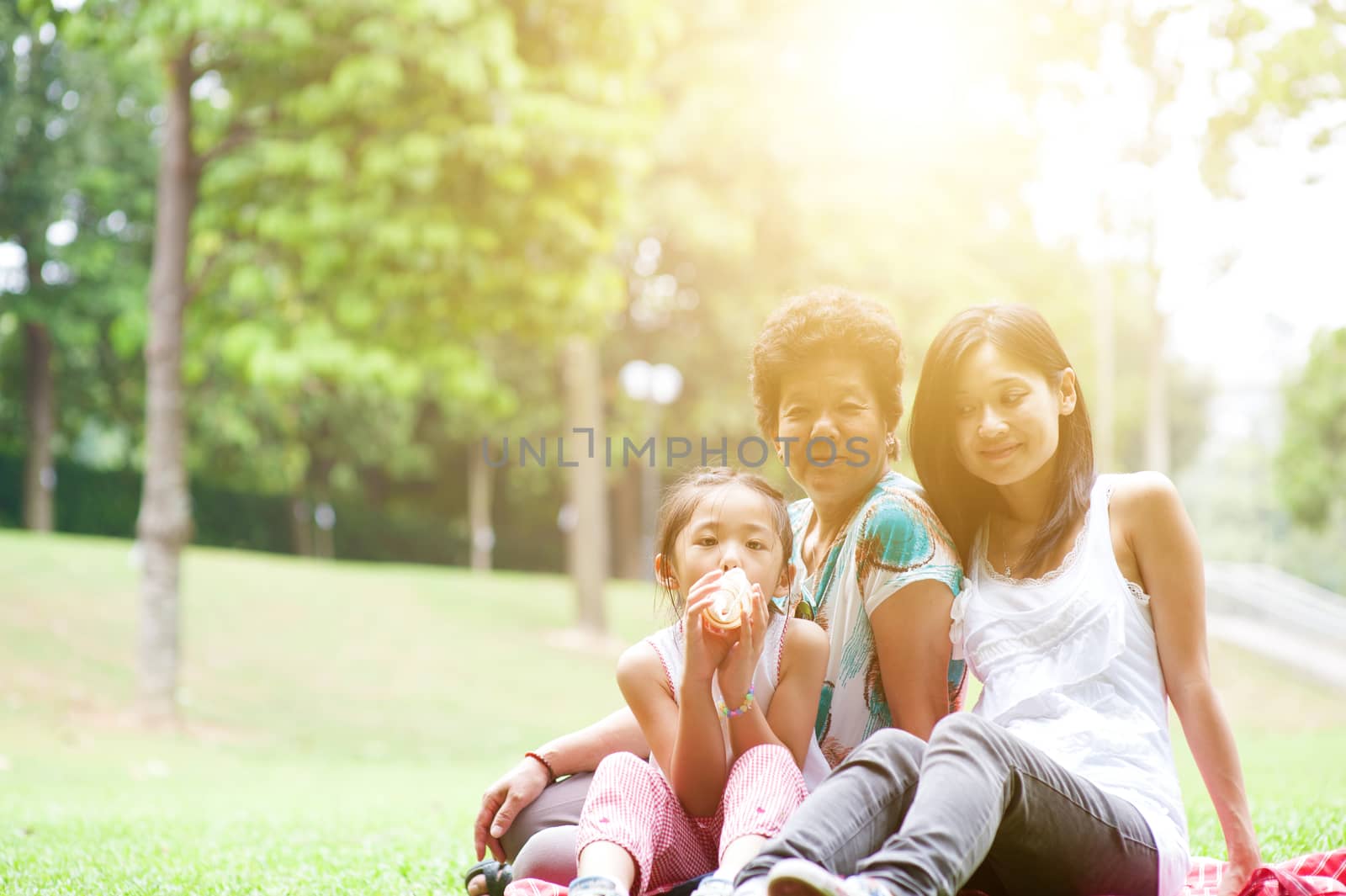 Portrait of multi generation Asian family at nature park. Grandmother, mother and daughter outdoor fun. Morning sun flare background.