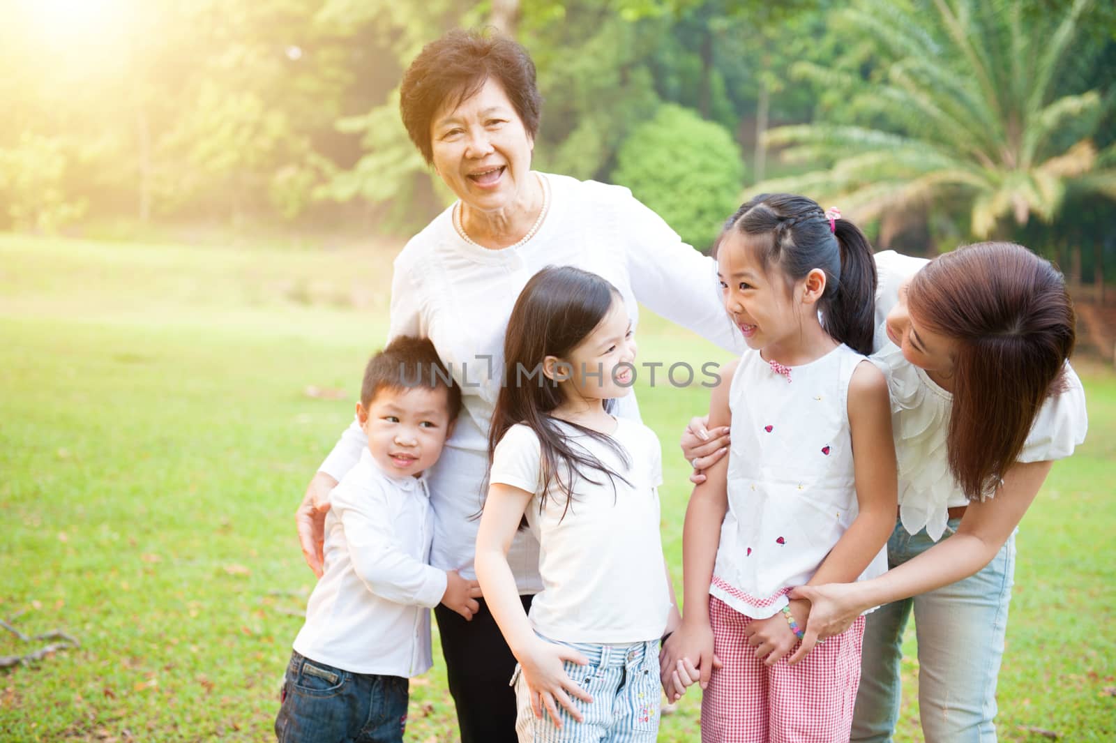 Portrait of multi generations Asian family at nature park. Grandmother, mother and grandchildren outdoor fun. Morning sun flare background.