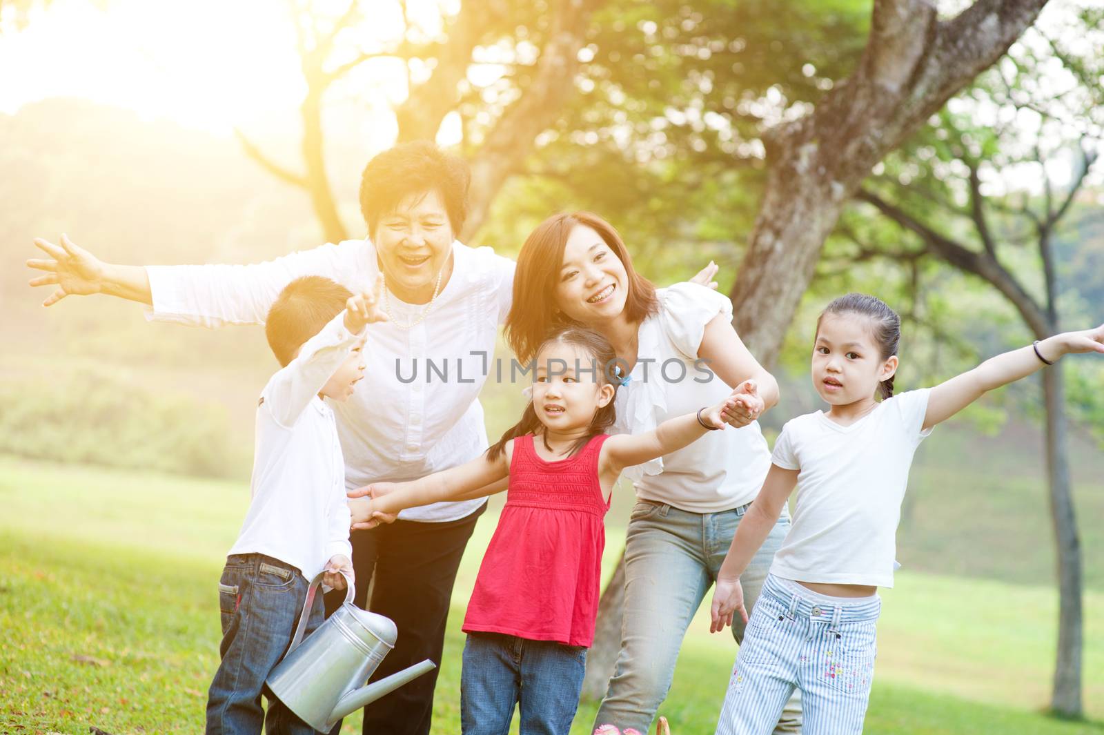 Candid portrait of happy multi generations Asian family at nature park. Grandmother, mother and grandchildren outdoor fun. Morning sun flare background.