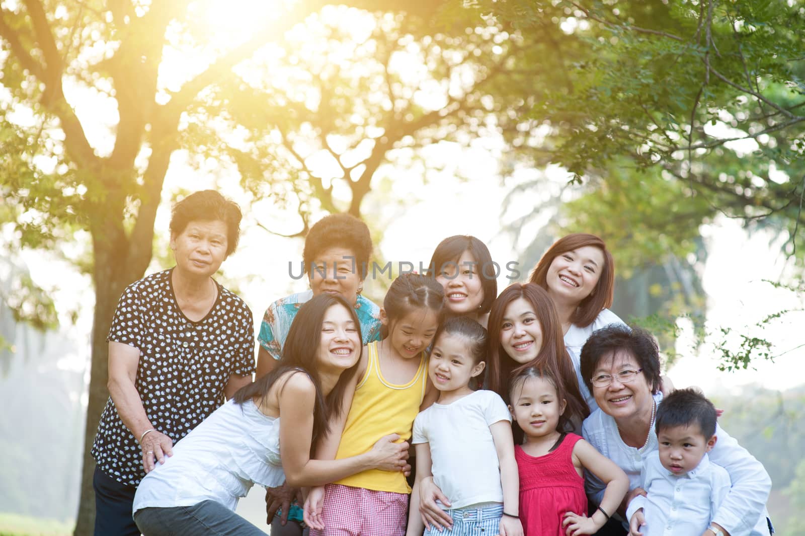 Large group of Asian multi generations family portrait, grandparent, parent and children, outdoor nature park in morning with sun flare.