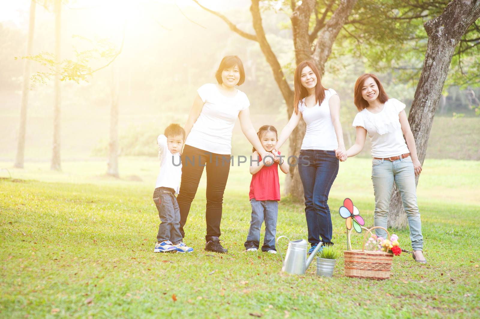 Asian family playing at nature park, parents and children, outdoor in morning with sun flare.