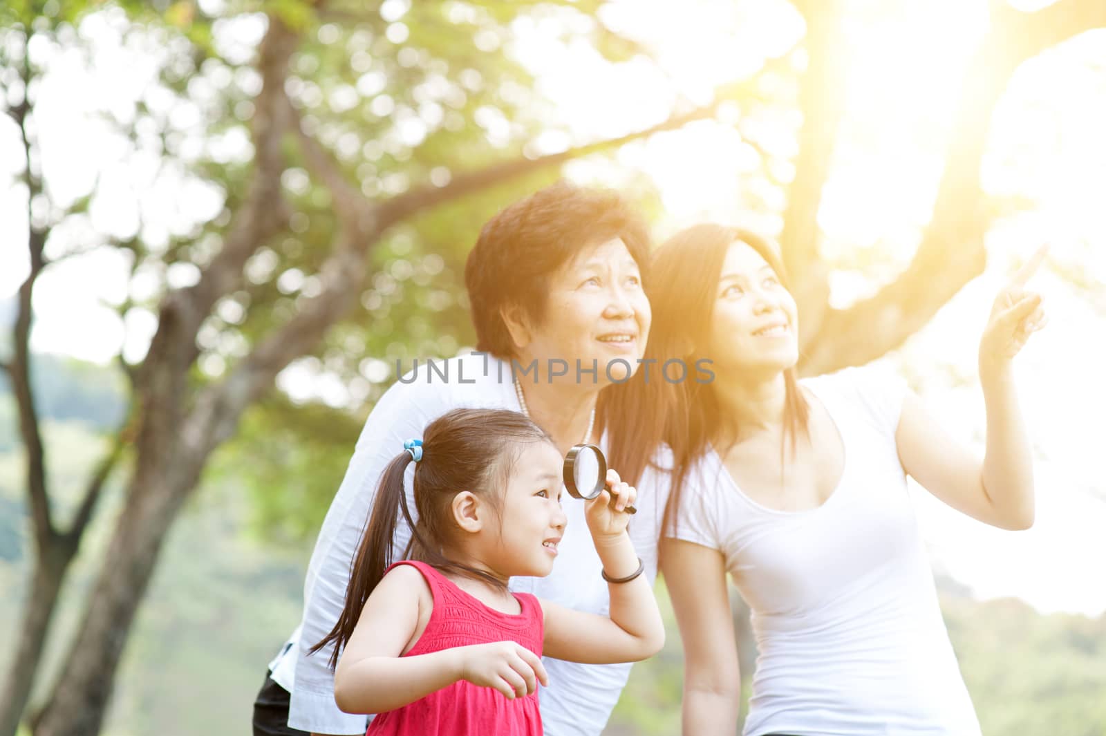 Portrait of multi generations Asian family at park. Grandmother, mother and daughter outdoor fun, exploring the nature. Morning sun flare background.