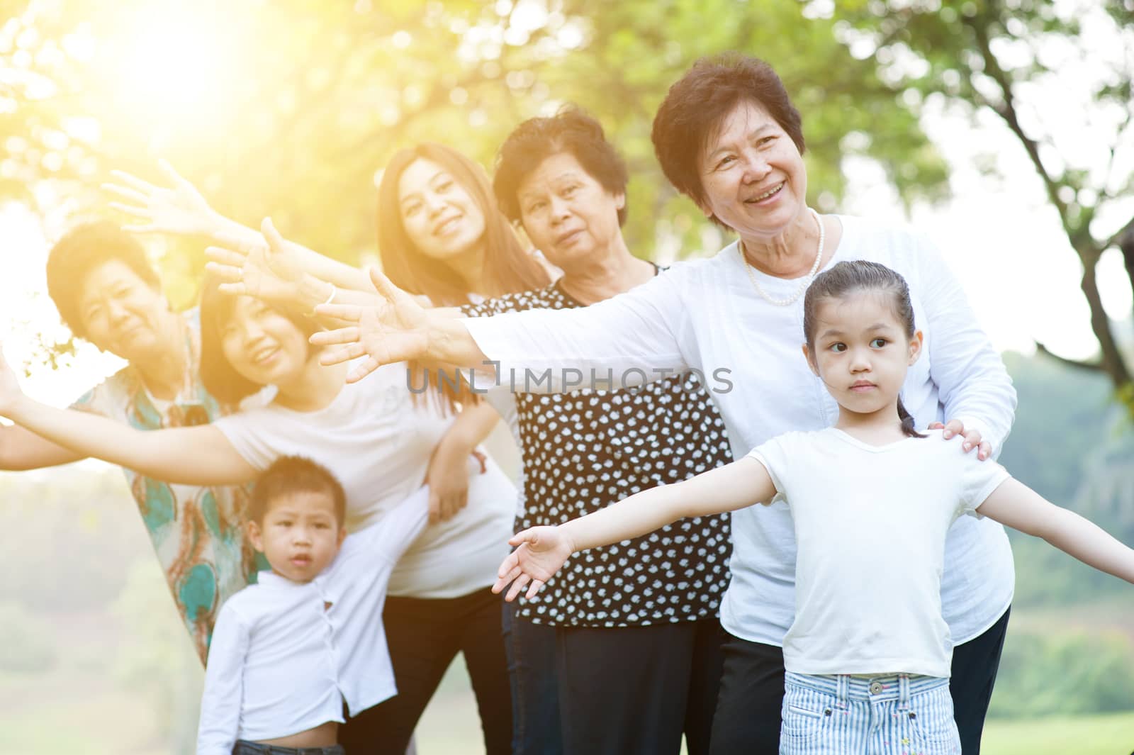 Big group of happy Asian multi generations family playing at park, grandparent, parent and children, outdoor nature park in morning with sun flare.