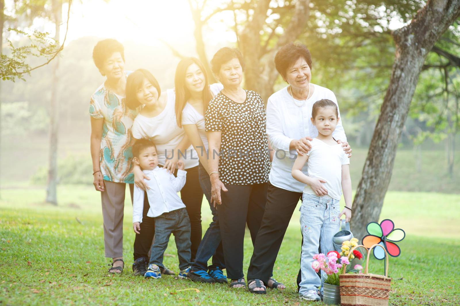 Large group of Asian multi generations family playing at park, grandparent, parent and children, outdoor nature park in morning with sun flare.