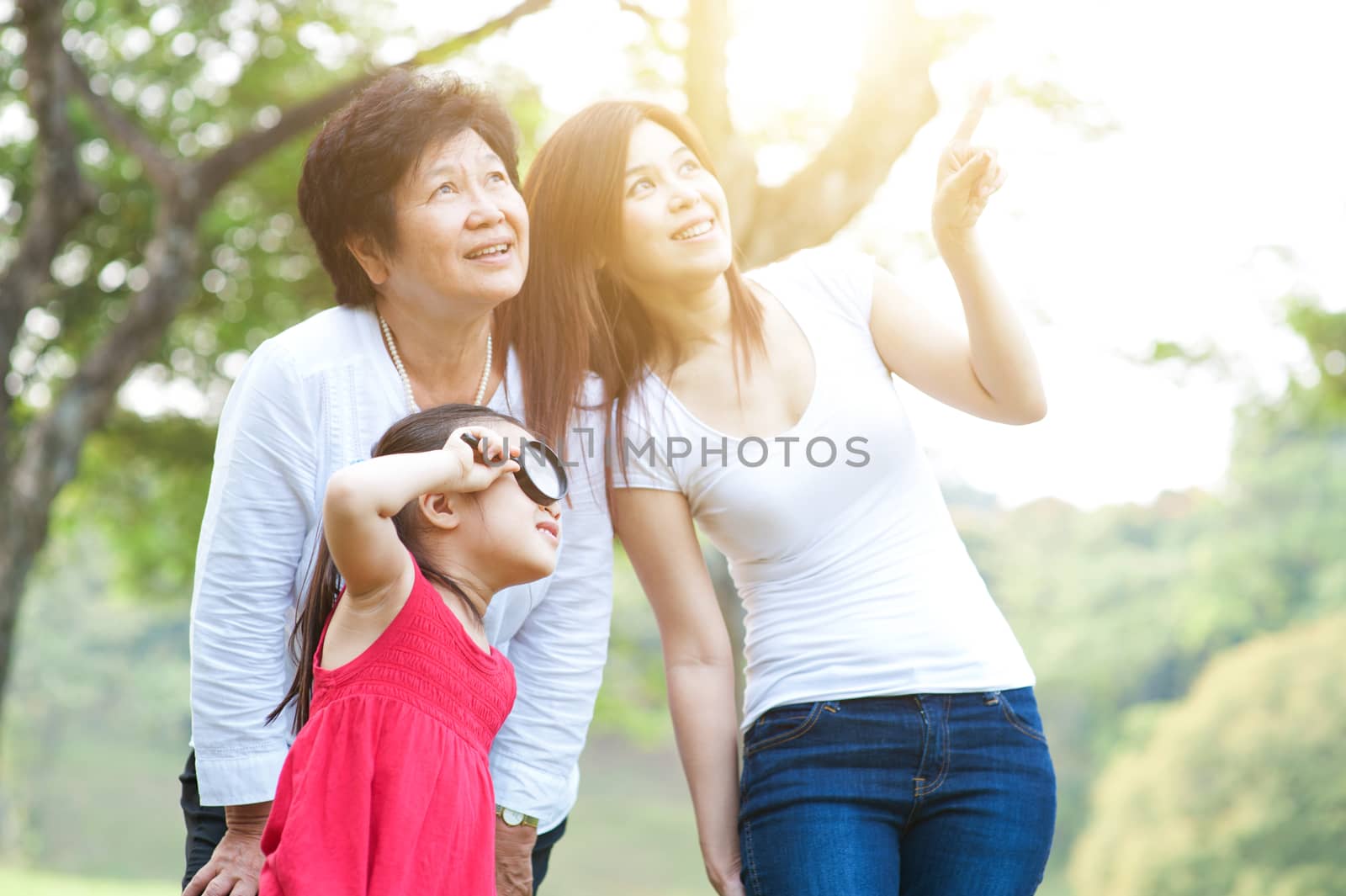 Portrait of happy multi generations Asian family at park. Grandmother, mother and daughter outdoor fun, exploring the nature. Morning sun flare background.