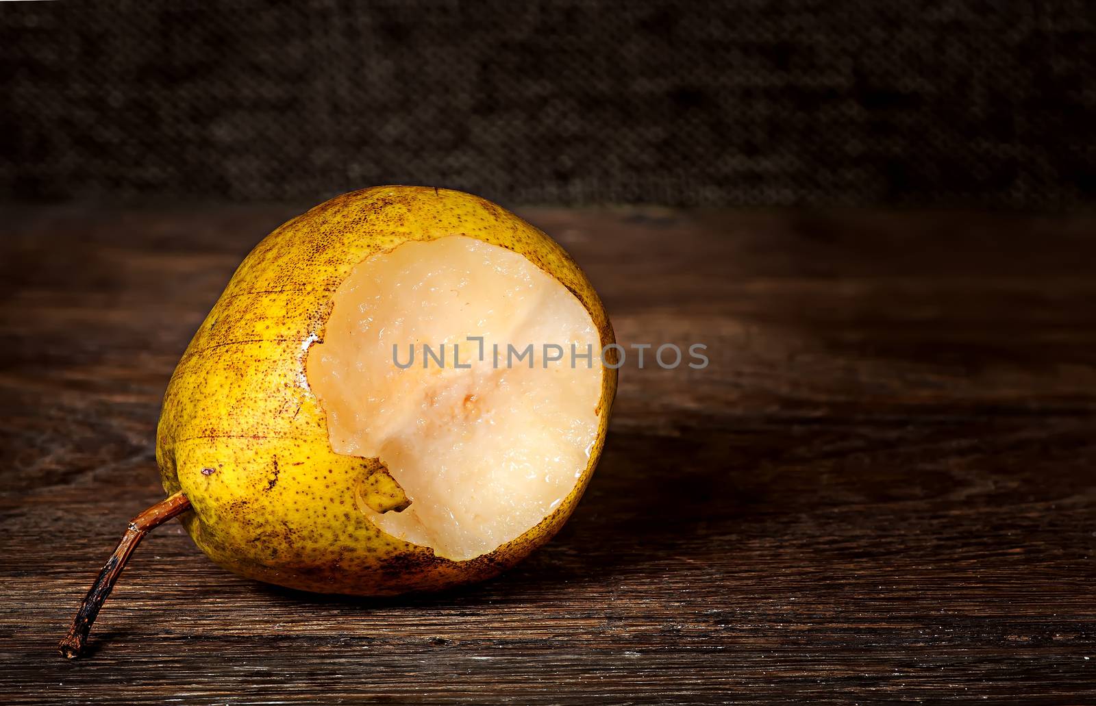 One bitten pear lying on a wooden table by Cipariss