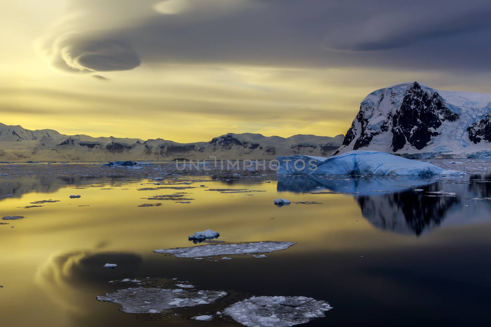 Blue iceberg, mountains and sunset reflecting in ocean at Lemaire Strait, Antarctica