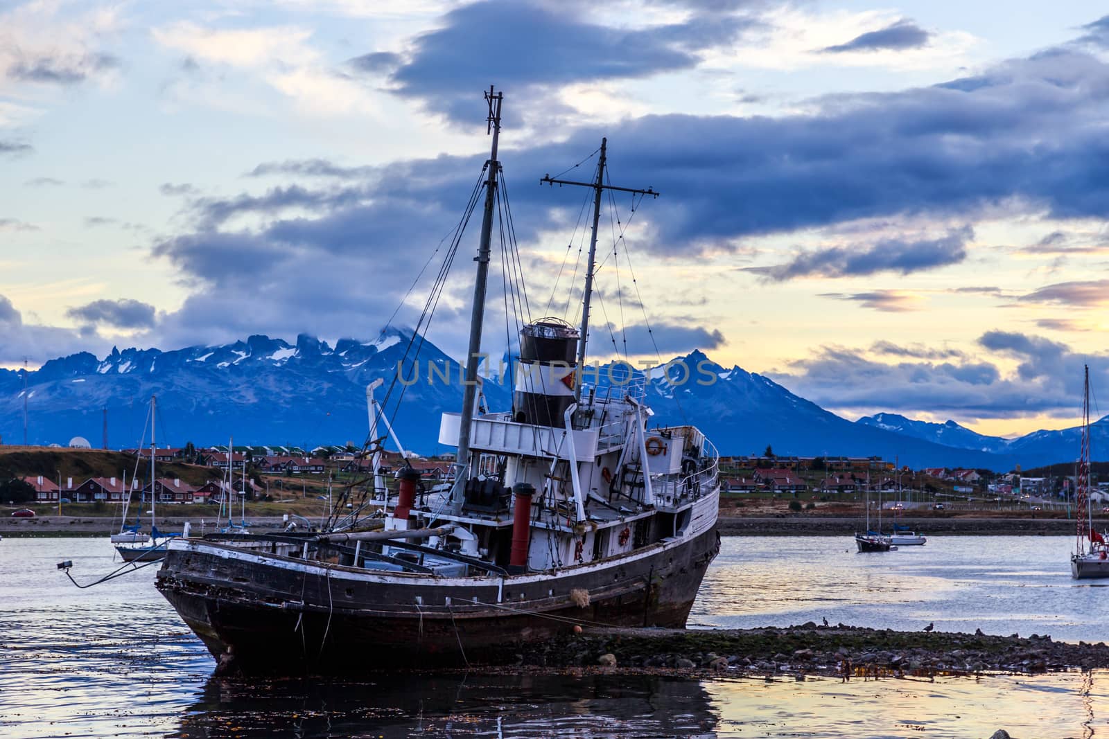 Old broken ship stranded ashore and village with mountains in the background, Ushuaia, Patagonia, Argentina