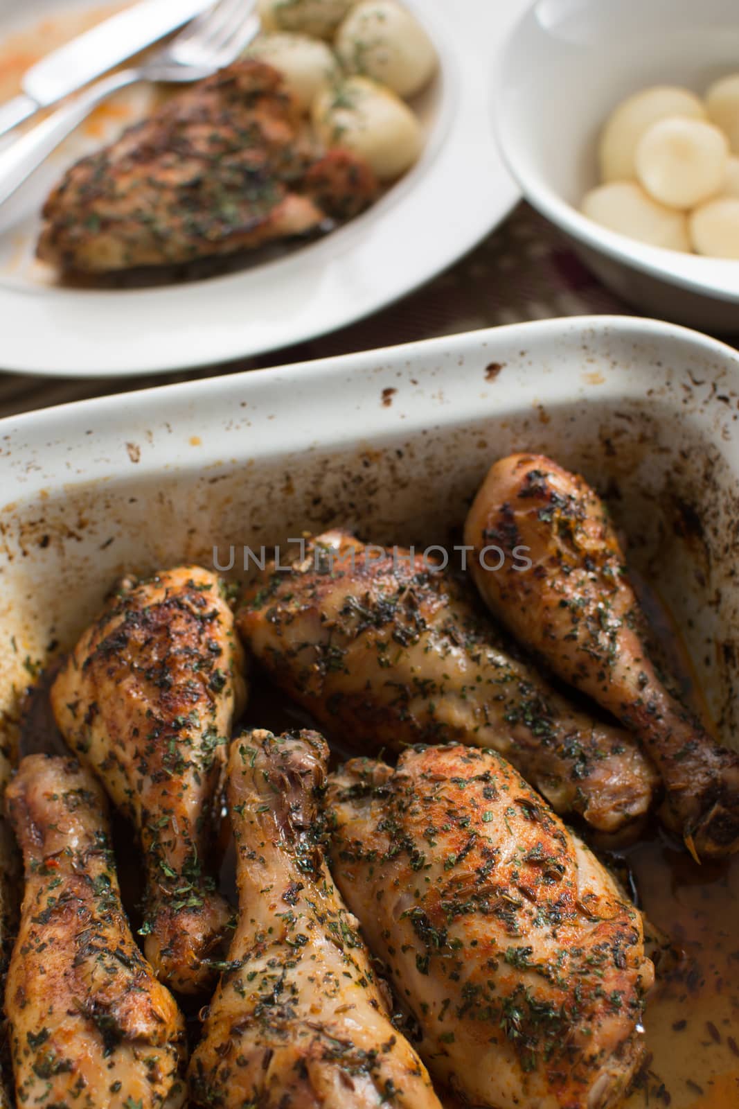 barbecued chicken drumsticks  with herbs in the baking dish with potatoes in the background