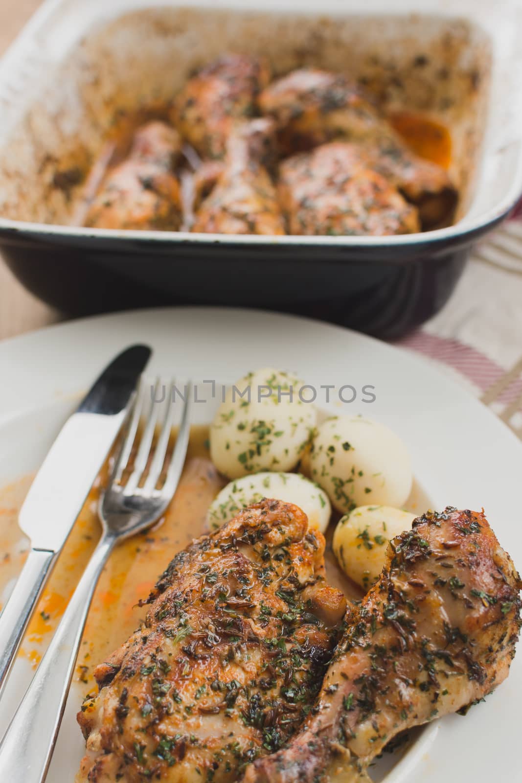 baked chicken drumsticks on a plate with potatoes, chicken in the oven dish with herbs