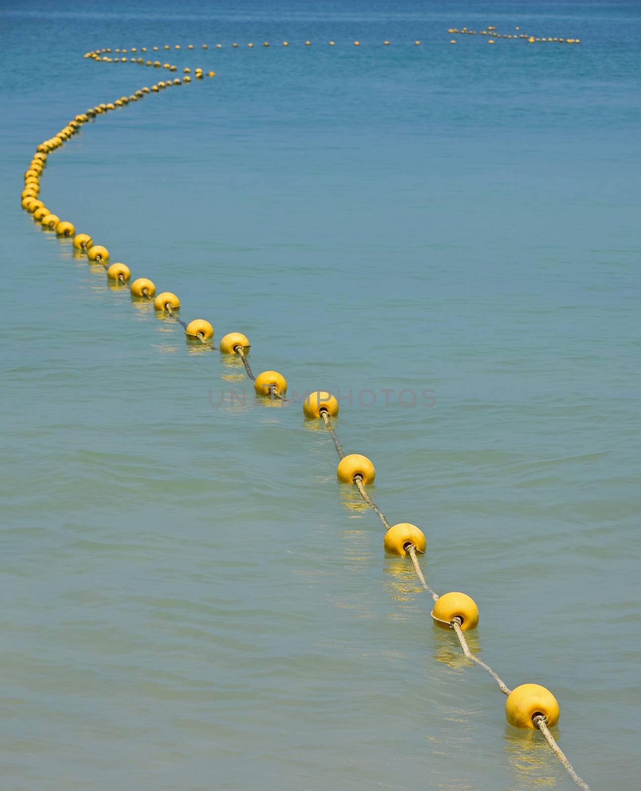 Chain of yellow polystyrene sea marker buoys with cable tow in blue sea water, in perspective