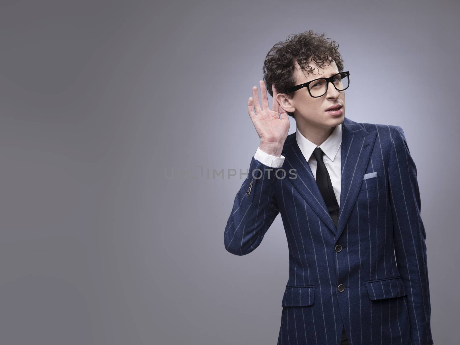 Young man cupping hand behind ear on gray background with copy space - what? cant hear you concept