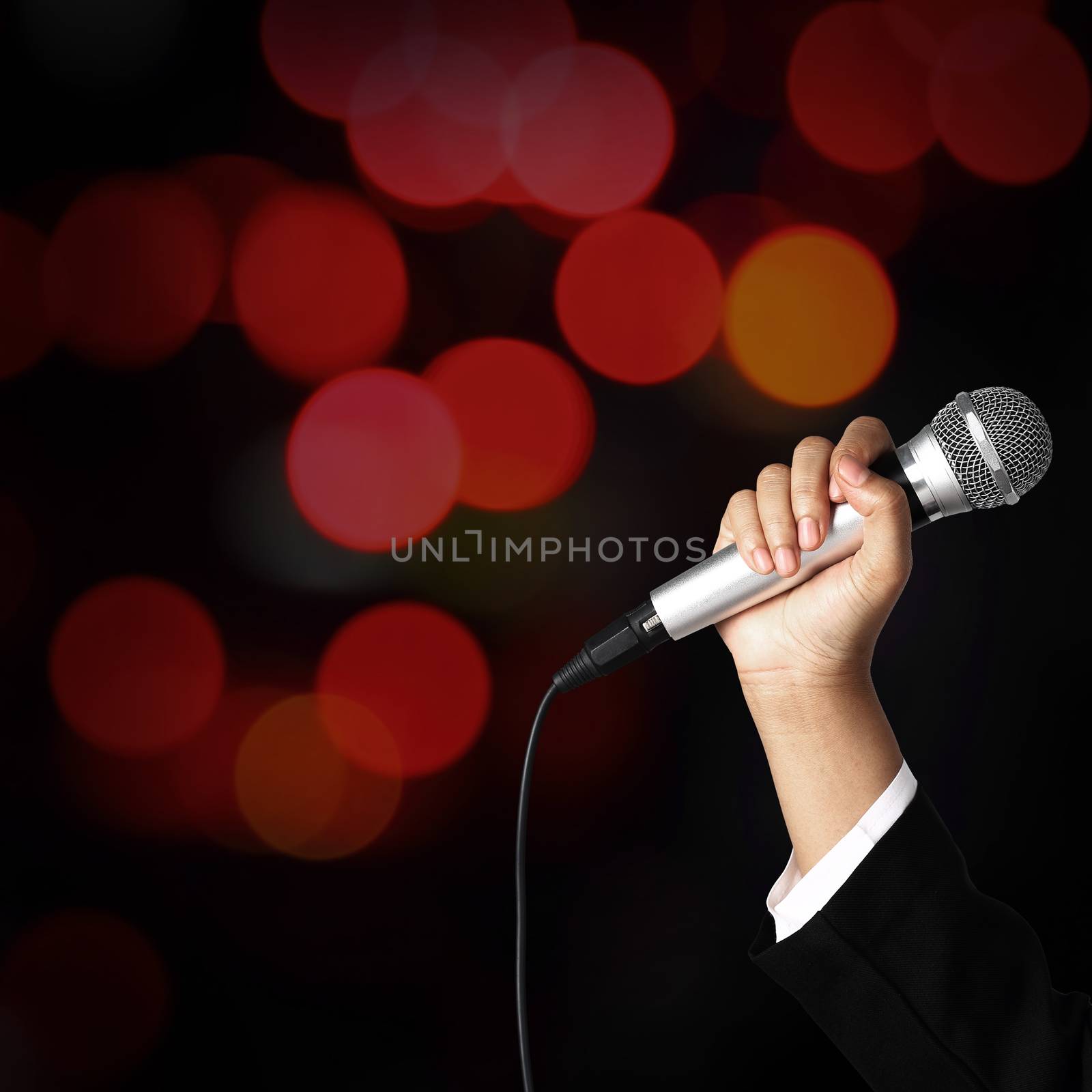 Businesswoman hand holding a microphone on blur of colorful bokeh background, seminar concept.