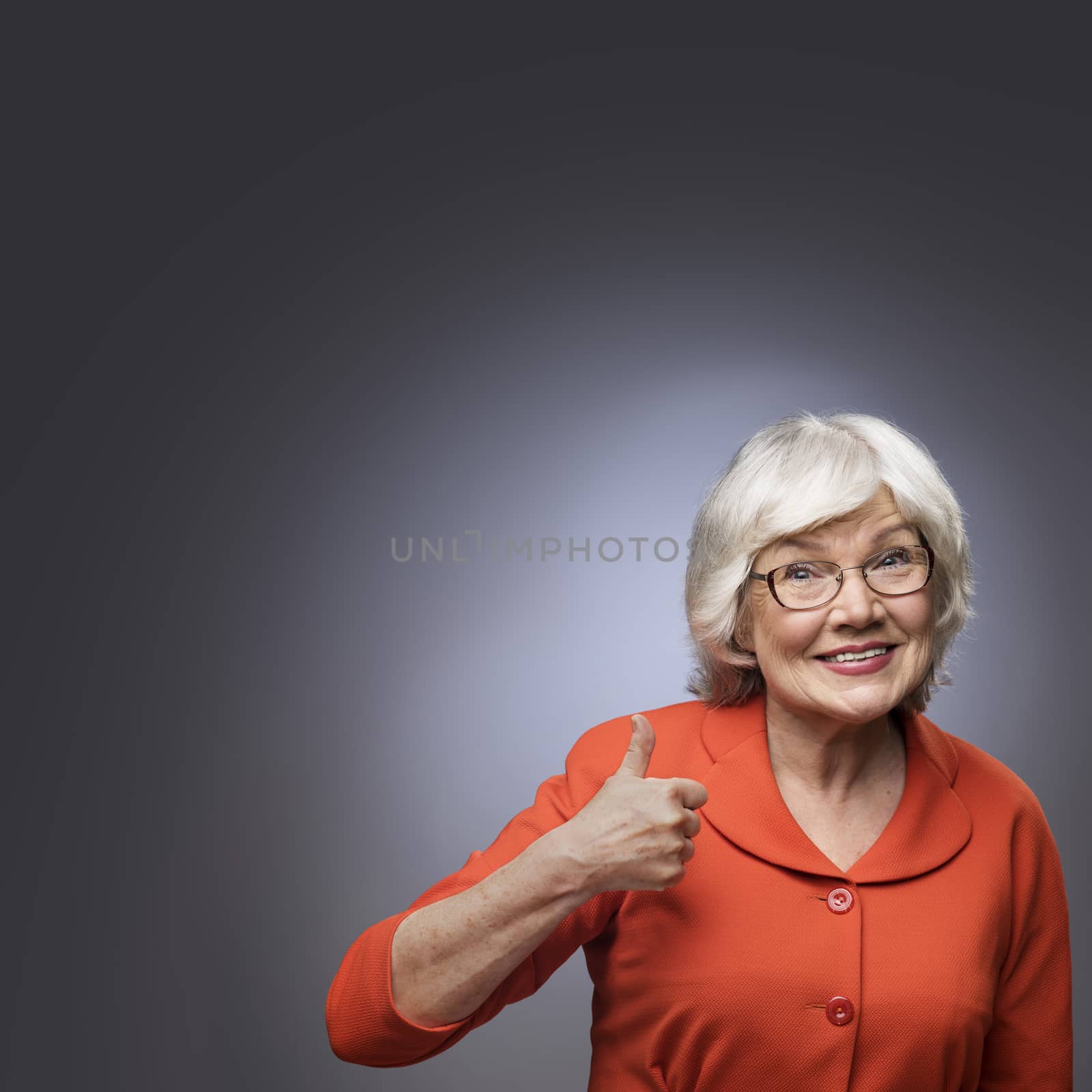 Smiling senior lady showing thumb up sign on gray background with copy space