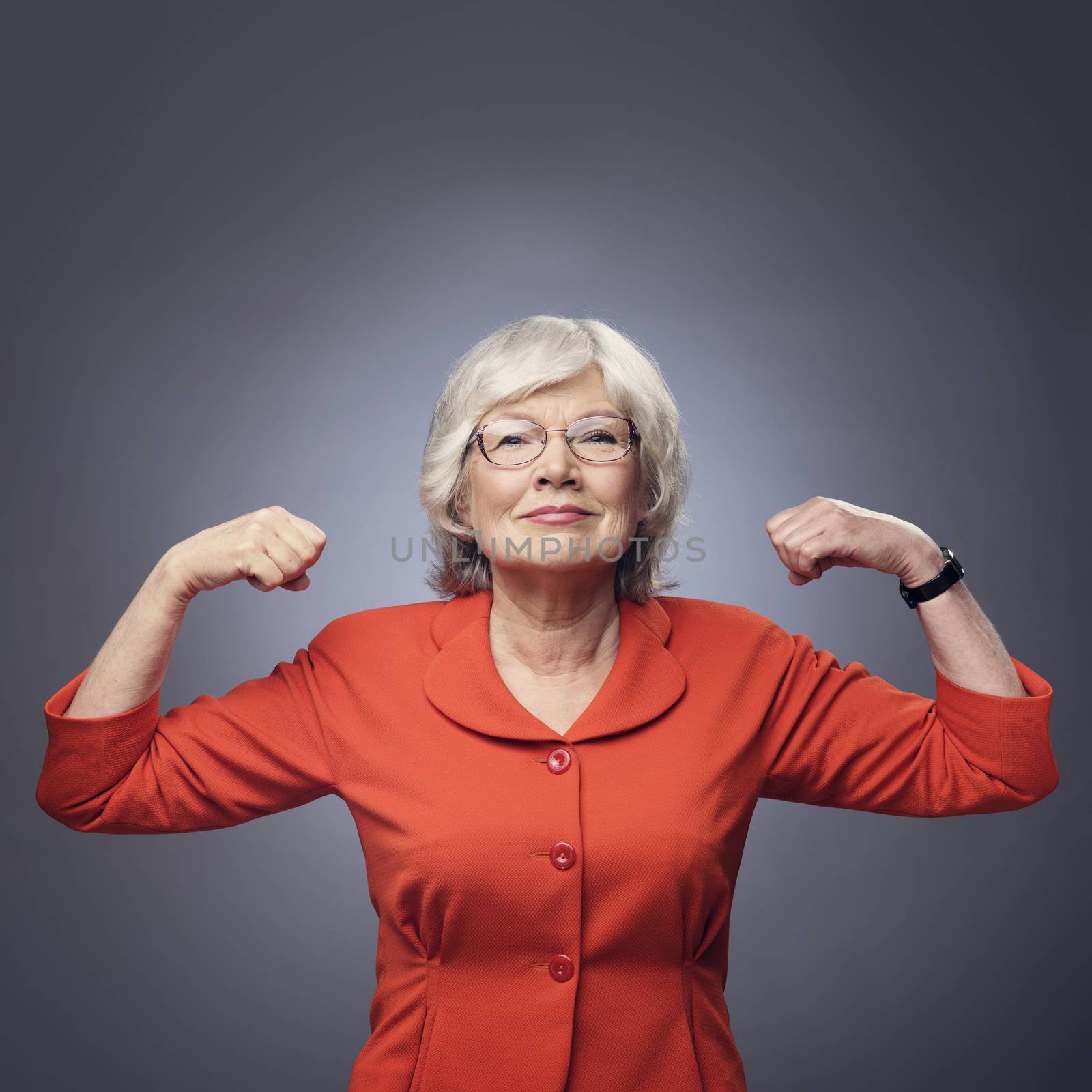 Smiling senior lady showing her muscles on gray background with copy space