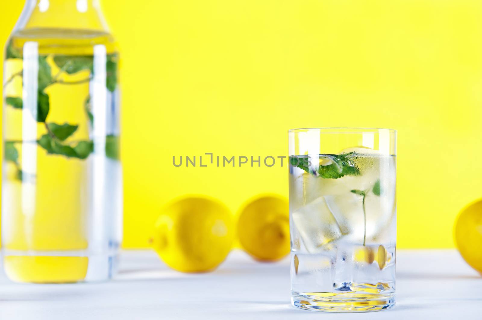 Cold water with lemon and mint on yellow background by Michalowski