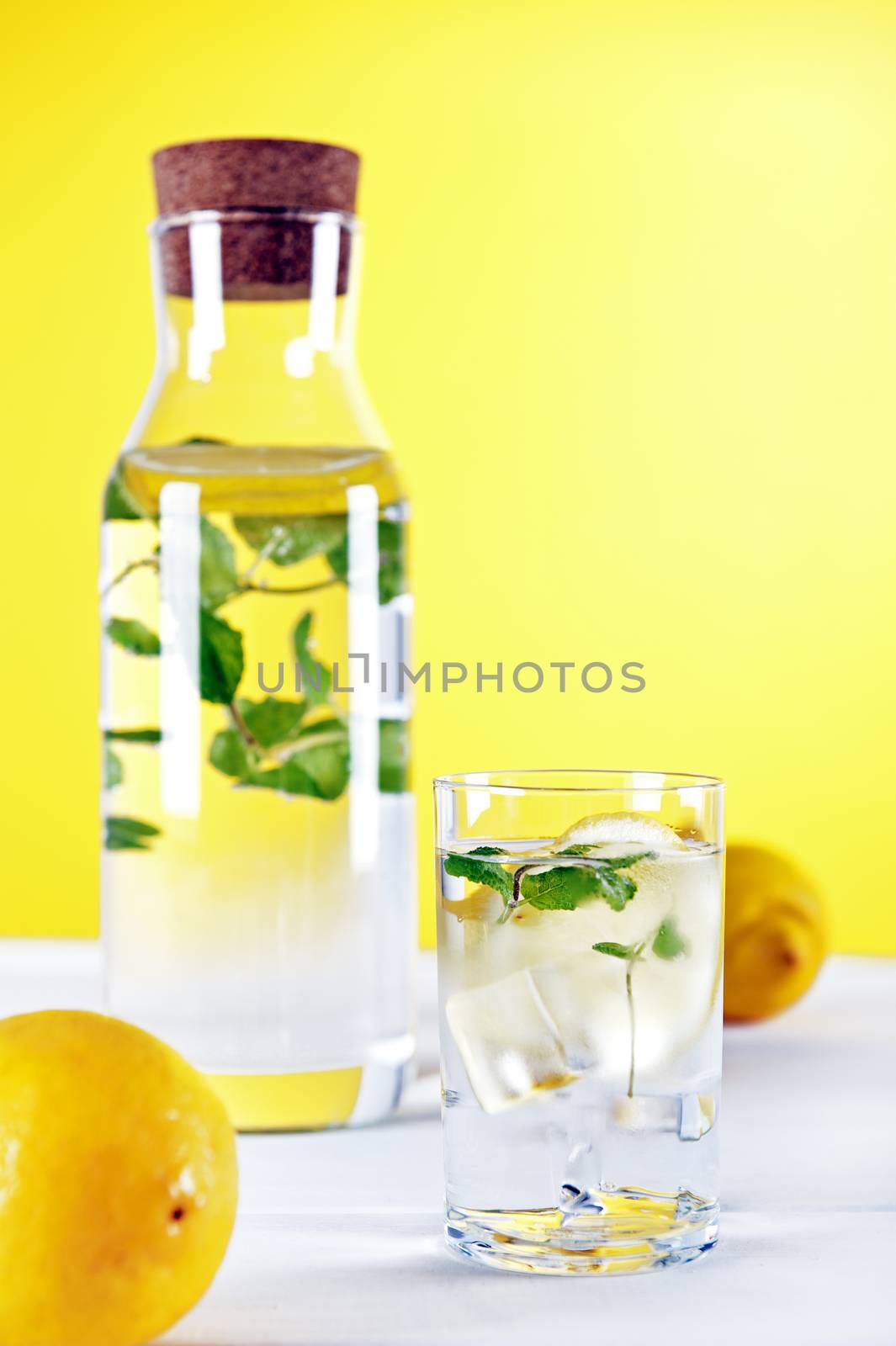 Cold water with lemon and mint on yellow background by Michalowski