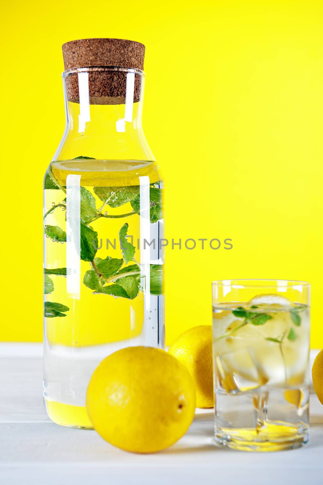 Cold water with lemon and mint on yellow background by Michalowski