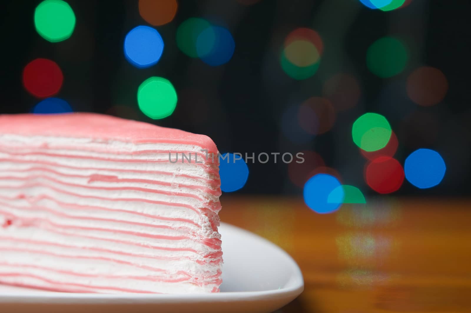 Close up crepe cake on white plate with wood table have colorful bokeh as background.