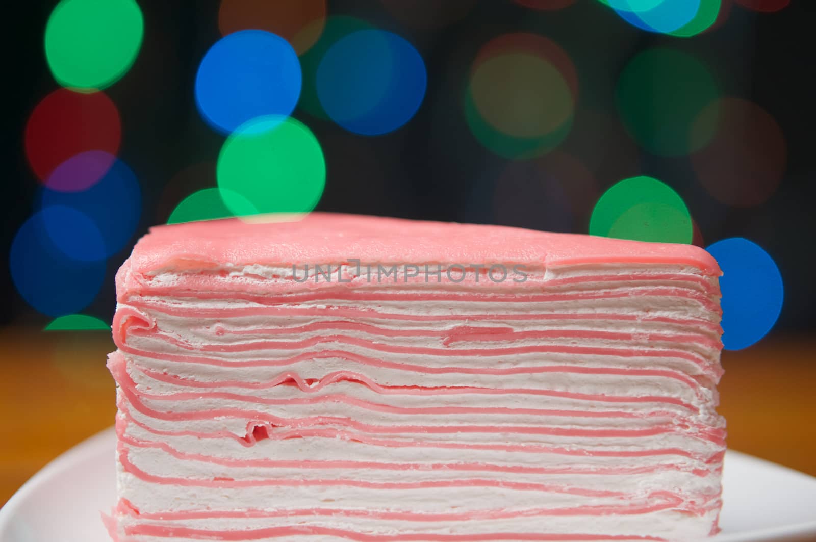 Crepe cake on white plate with wood table have colorful bokeh as background.