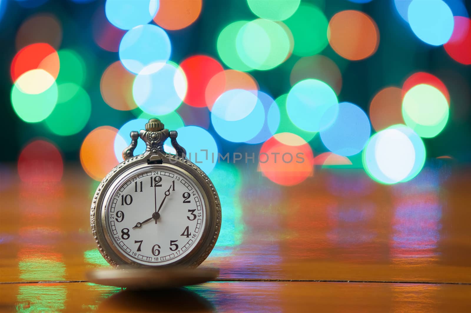 Old vintage clock on wood table have colorful bokeh as background.