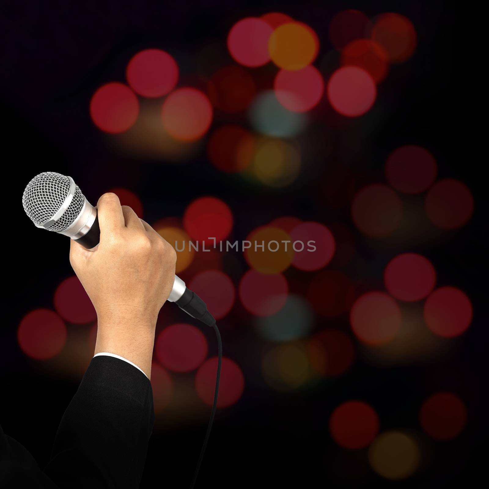 Businesswoman hand holding a microphone on blur of colorful bokeh background, seminar concept.